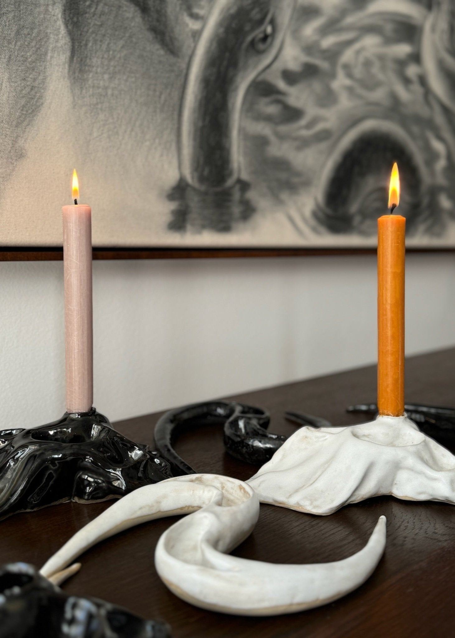Composition of a black and a white candleholder with candles light inside as well as a black and a white ceramic artwork designed by Aline Schwörer