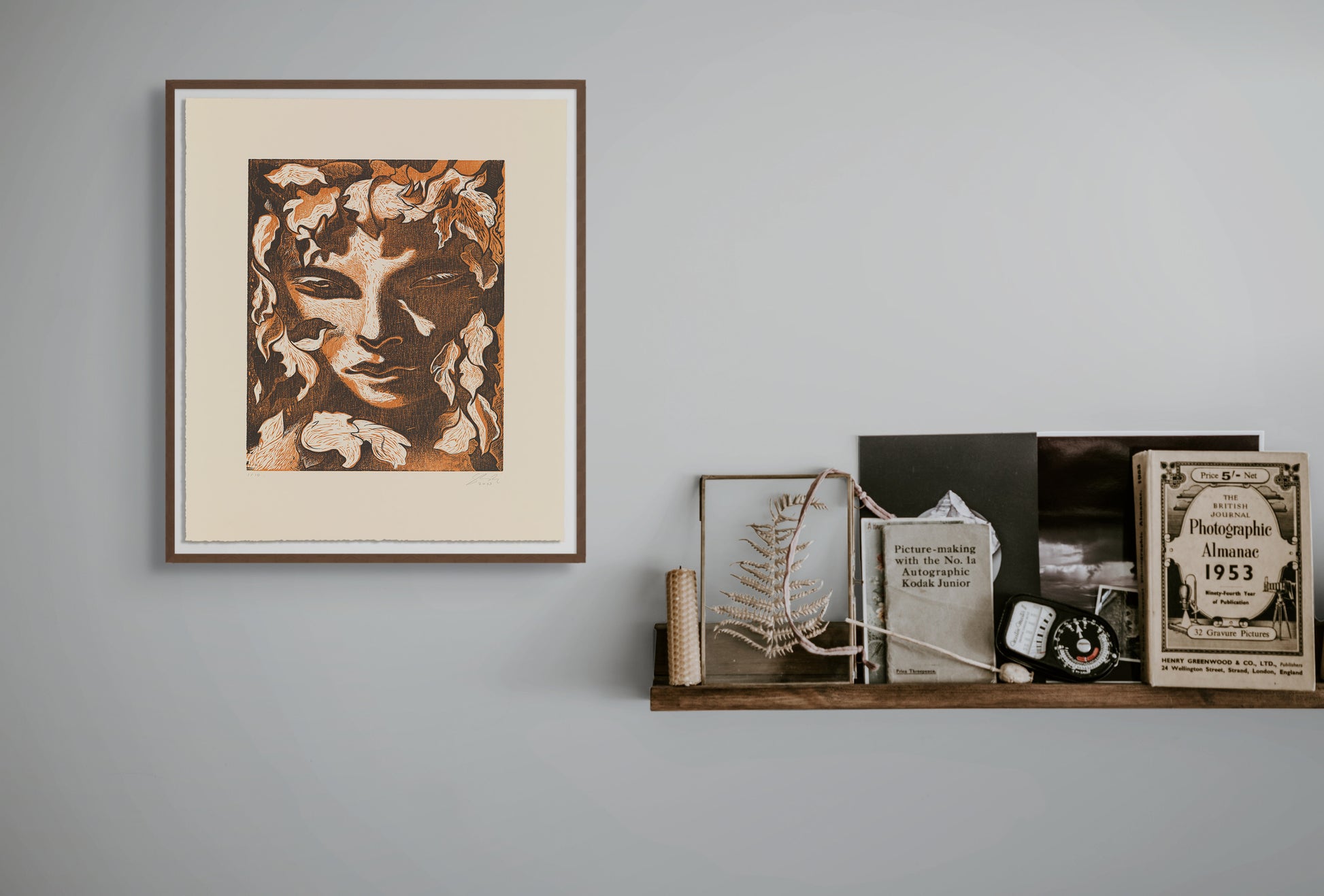 Framed artwork on a wall with a shelf displaying books and decorative items.