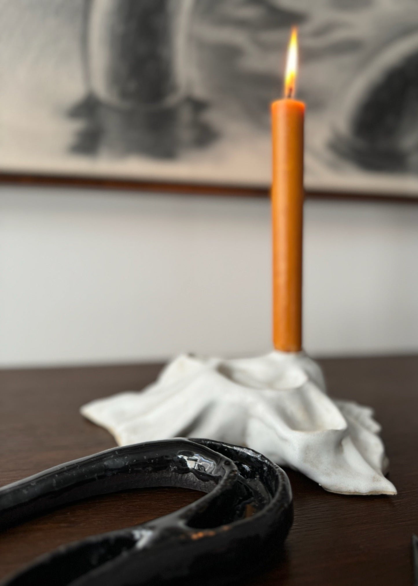 Detail of a black ceramic artwork shaped like a snake with a white candleholder in the background - designed by Aline Schwörer