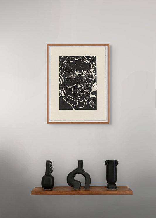 Framed black and white portrait by Elizabeth Peyton on a gray wall with three black sculptures on a wooden shelf below.