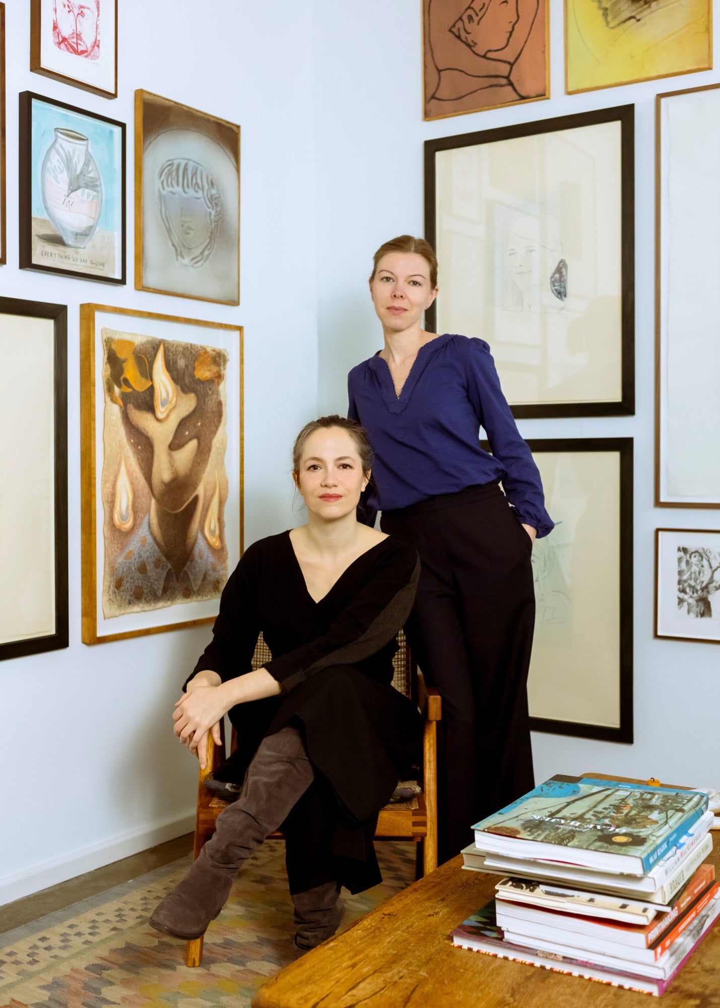 Photograph of the two founders of FRIDAY BIRD gallery - Nora Vogel (standing) and Nicola Petek (sitting) - in their gallery room surrounded by pictures.