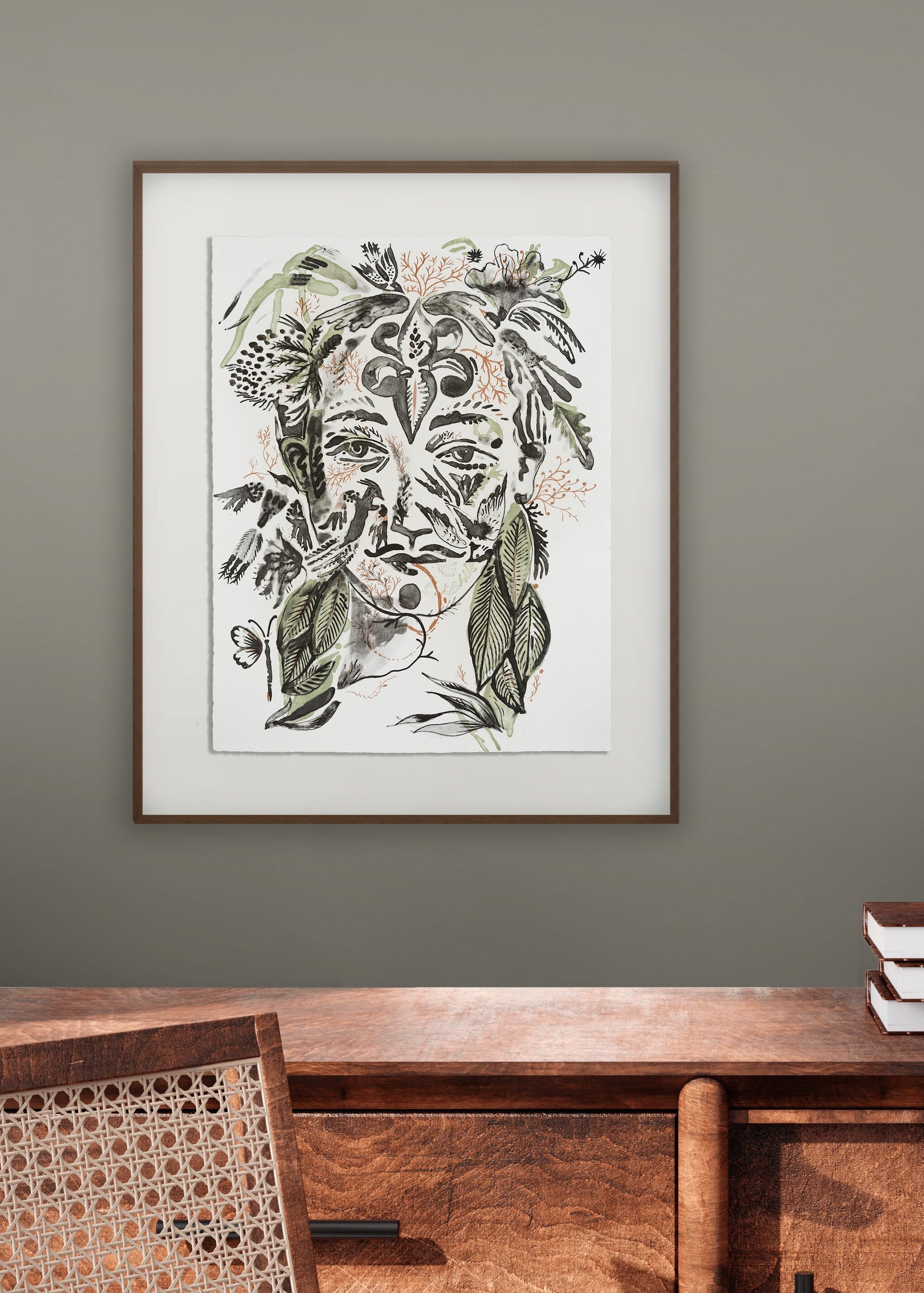 Framed artwork by artist and illustrator Olaf Hajek of a stylized face with floral elements on a wall above a wooden console table.