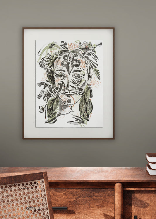 Framed artwork by artist and illustrator Olaf Hajek of a stylized face with floral elements on a wall above a wooden console table.
