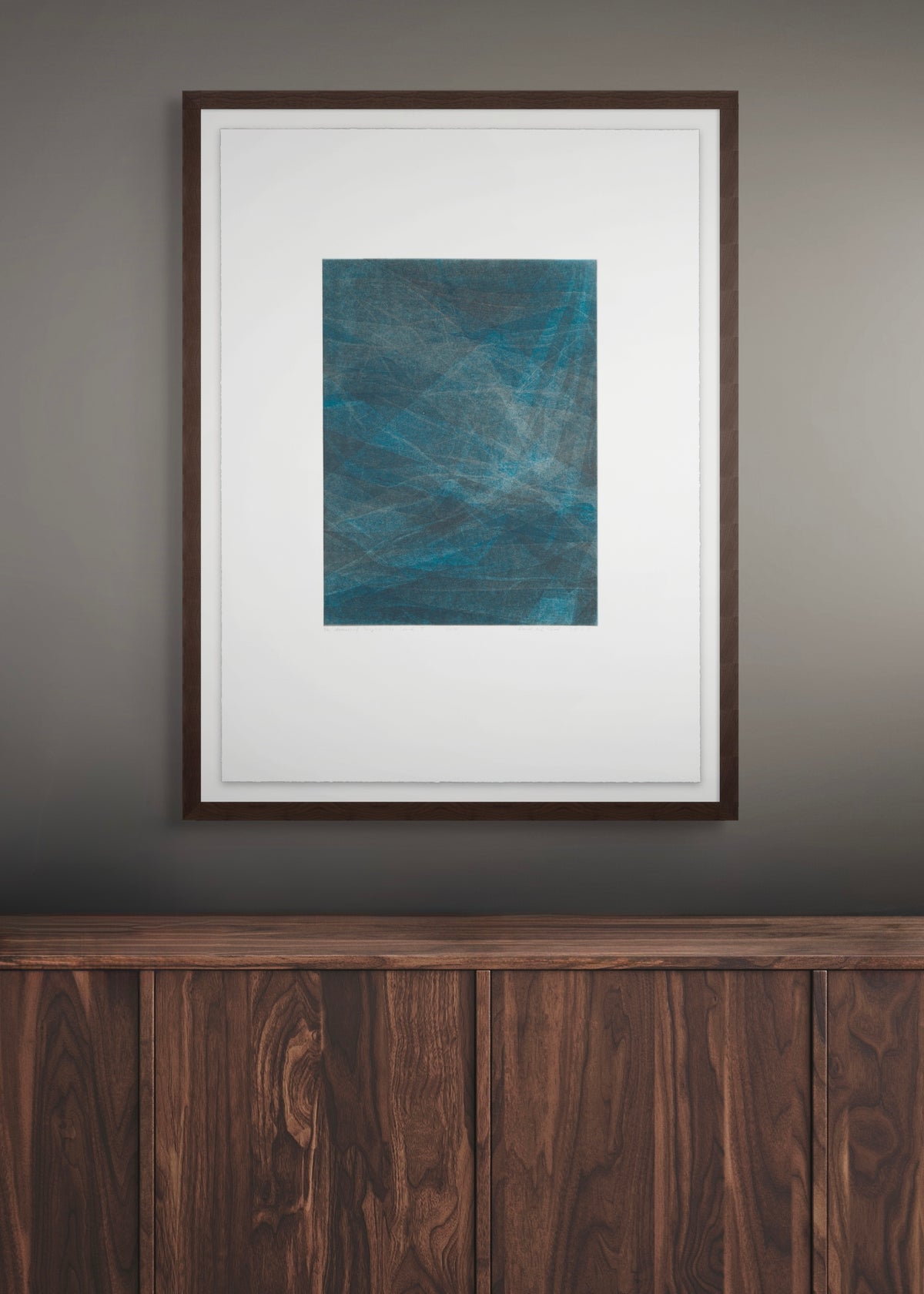 Framed abstract artwork by Daniel M. Schaal on a wall above a wooden piece of furniture.