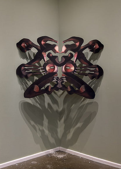 An art gallery room showing five framed abstract figurative artworks mounted on pale green walls, including a central black sculptural piece casting a shadow on the wall.