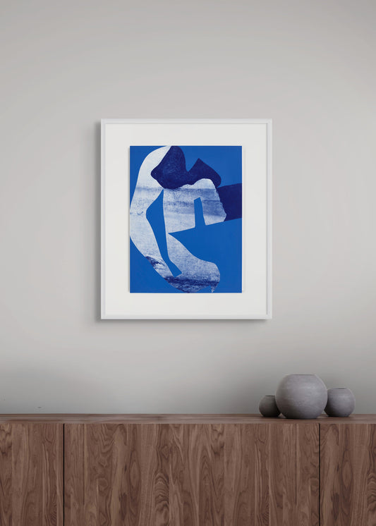 Framed abstract etching on a grey wall above a wooden cabinet with vases. 