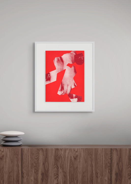 Framed artwork with a red background on a gray wall above a wooden shelf.