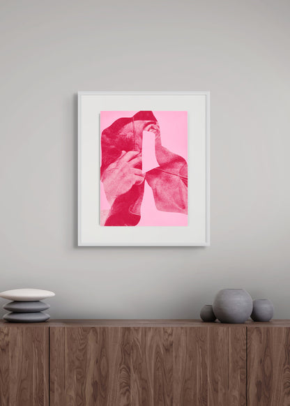 Framed pink abstract artwork by Arturo Herrera on a gray wall above a wooden shelf with decorative items.