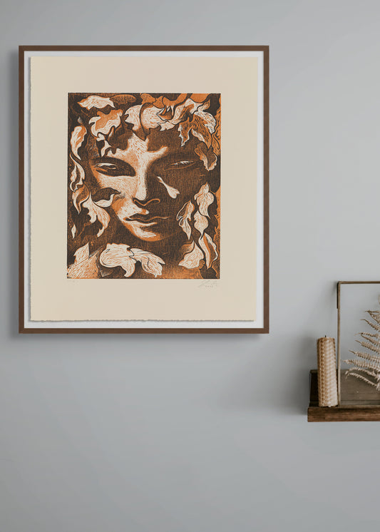 Framed artwork by Dennis Scholl of a face with floral elements on a gray wall.