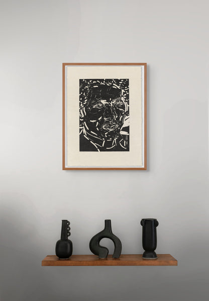Framed black and white portrait by Elizabeth Peyton on a gray wall with three black sculptures on a wooden shelf below.