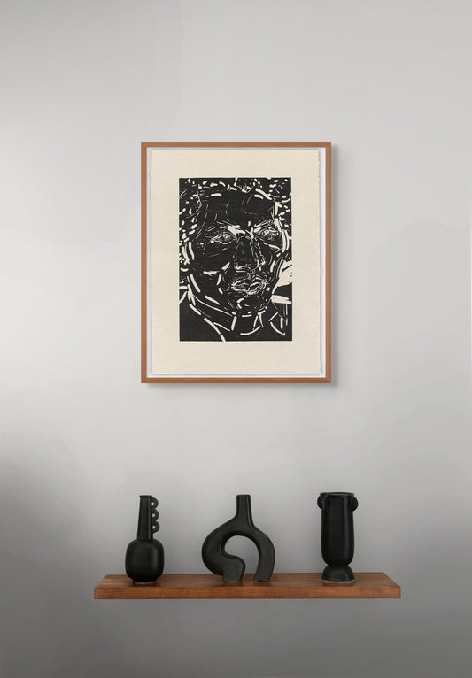 Framed black and white portrait by Elizabeth Peyton on a gray wall with three black sculptures on a wooden shelf below.
