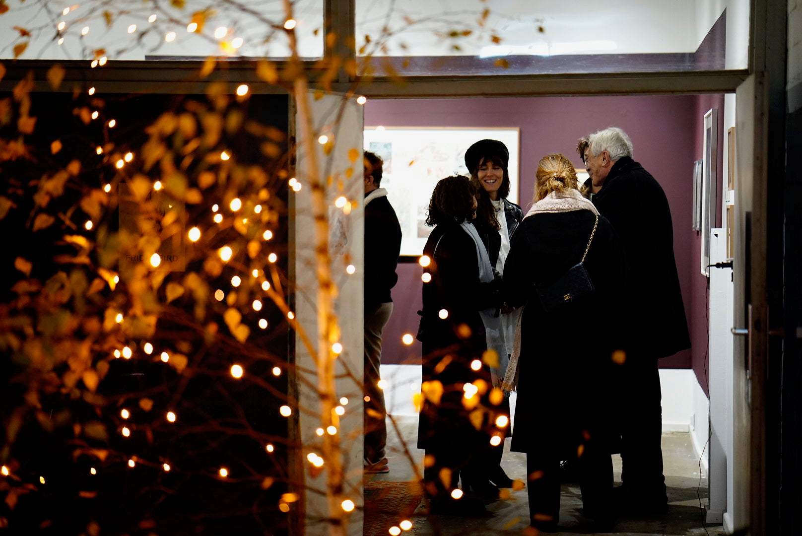 Group of people standing in Friday Bird Gallery with decorative lights and a red wall.