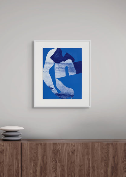 Framed abstract art print by Arturo Herrera in blue and white on a gray wall above a wooden cabinet.