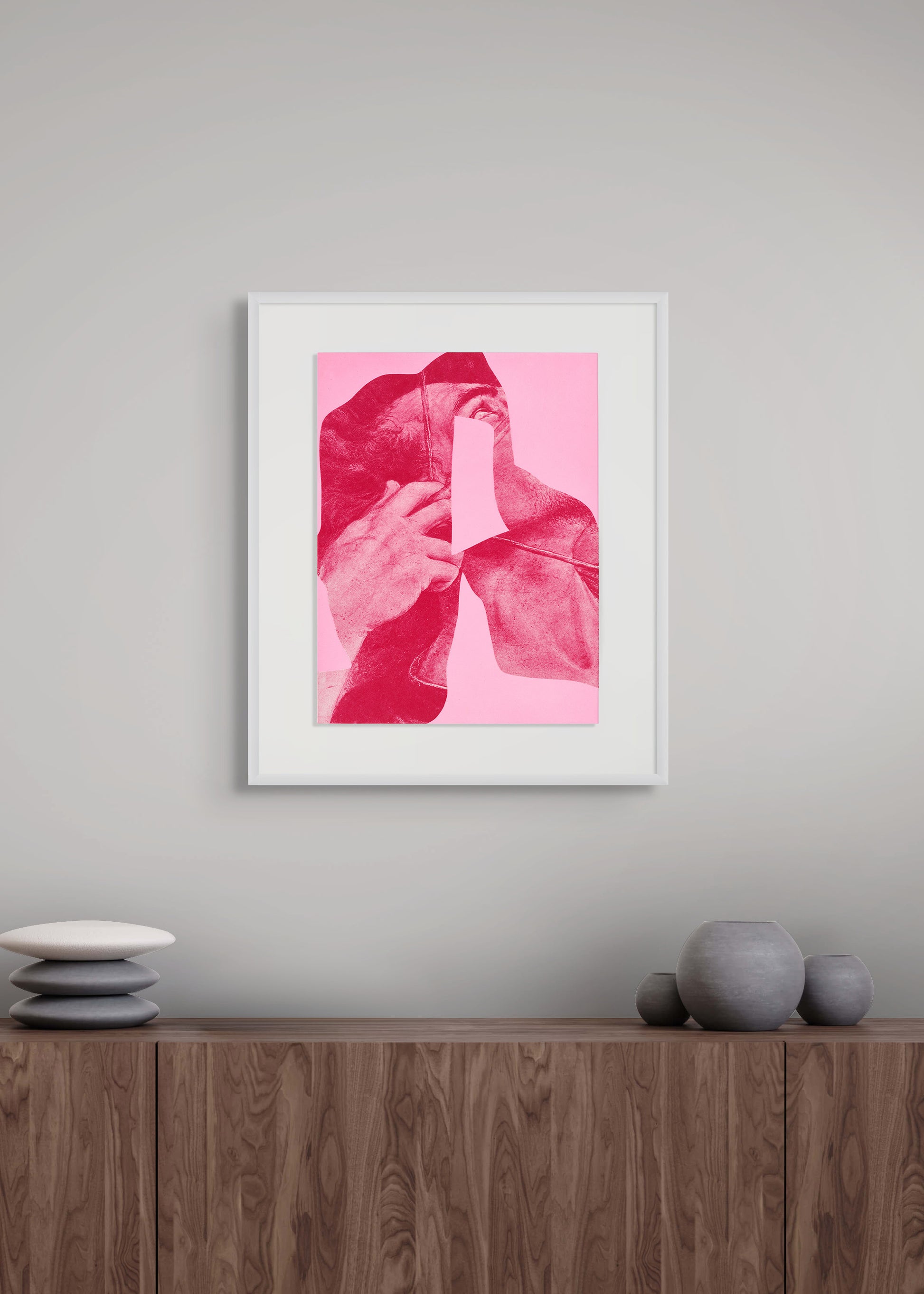 Framed artwork by Arturo Herrera with a pink and red abstract design on a gray wall above a wooden cabinet.