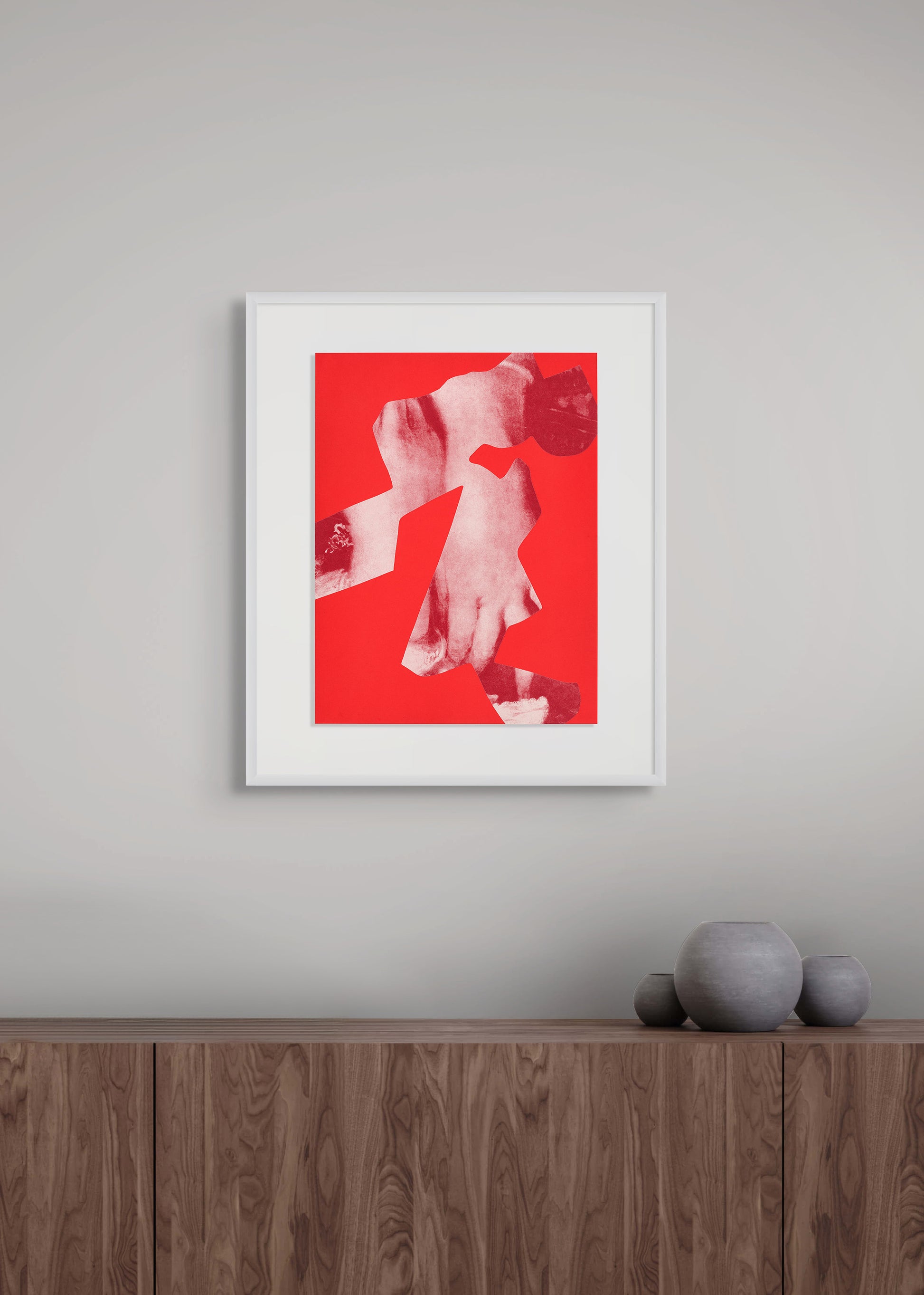 Framed artwork by Arturo Herrera with a red background and white abstract design on a gray wall above a wooden shelf.