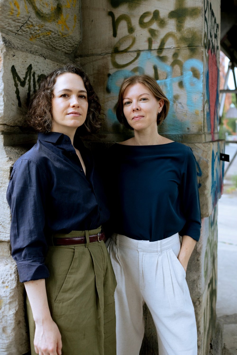 The two founders of Friday Bird, Nicola Petek and Nora Vogel, standing outside in front of wall with graffiti in Berlin.