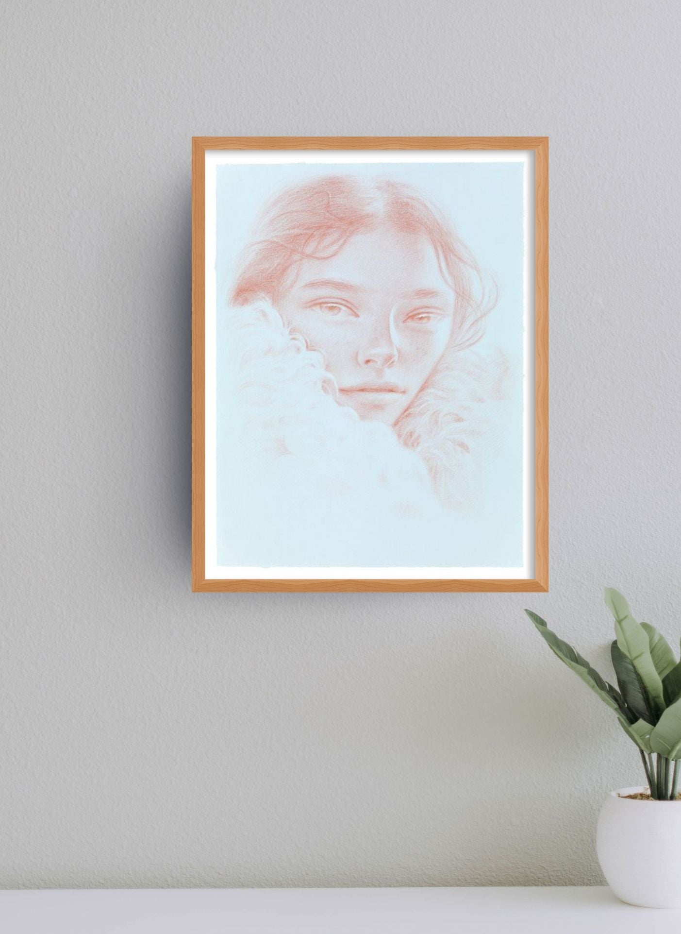 Framed artwork of a face on a wall with a plant below