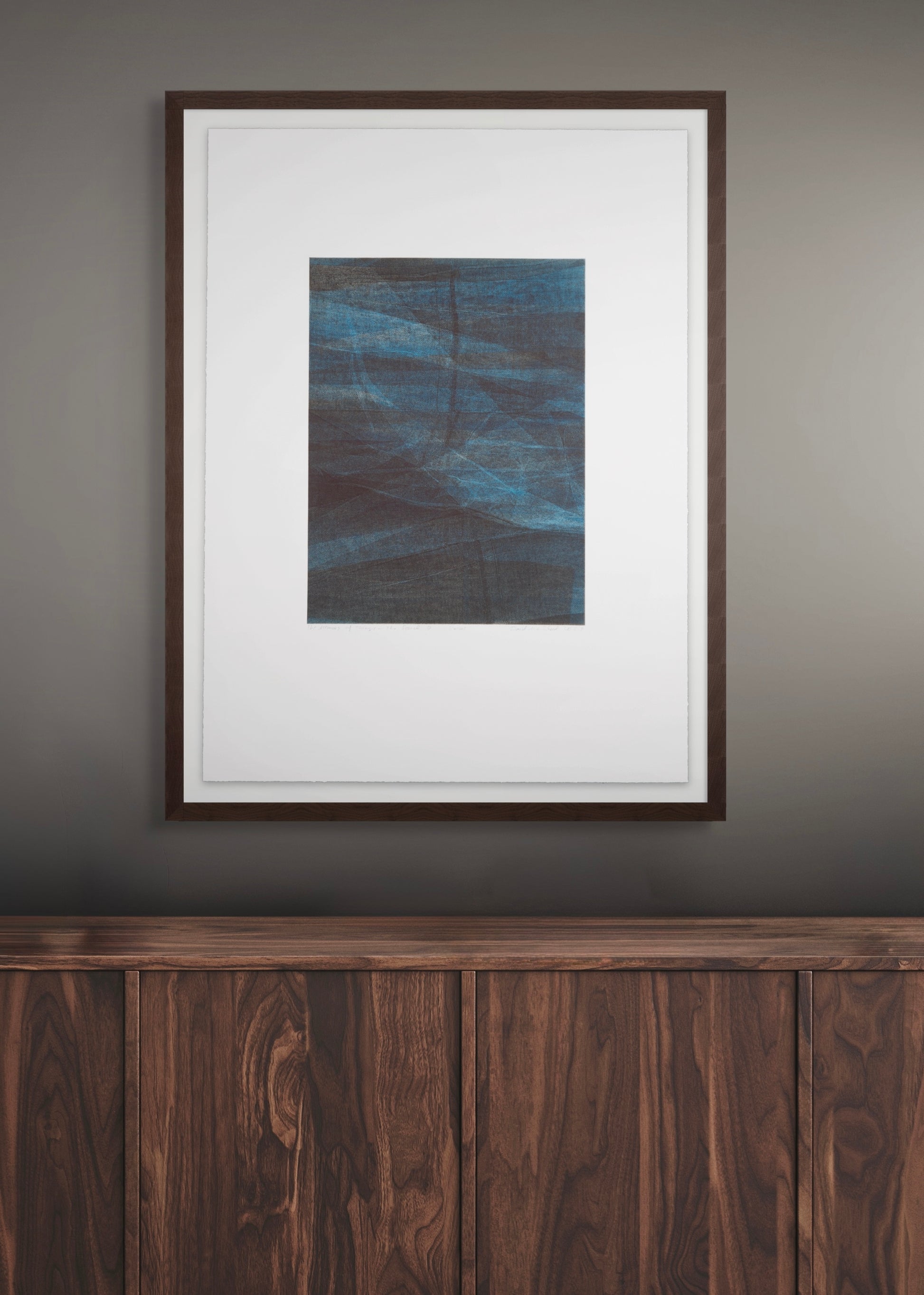 Framed abstract artwork by Daniel M. Schaal on a wall above a wooden piece of furniture.
