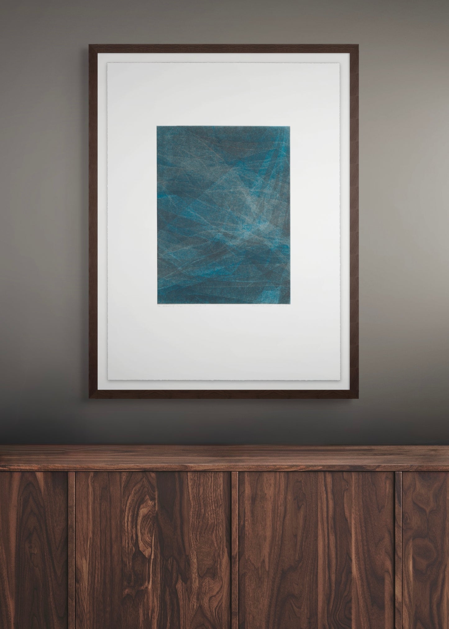Framed abstract artwork by Daniel M. Schaal on a wall above a wooden piece of furniture.