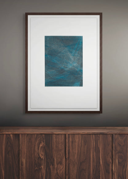 Framed abstract artwork by Daniel M. Schaal on a wall above a wooden piece of furniture.